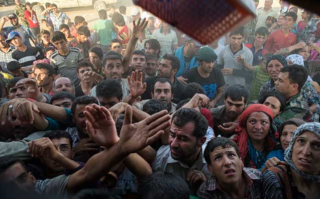 Syrian refugees who have arrived recently reach for clothes and other items distributed at the Kawergost camp outside of Erbil, Iraq, Aug. 20, 2013. (Photo: Lynsey Addario / The New York Times)